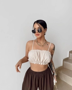 Detail of beige ruffled strapless camisole top paired with deep brown wide-leg trousers
