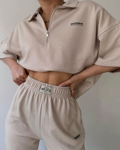 Detail of oat-colored two-piece set featuring half-zip collar and lettered embroidery