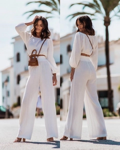 Detail of white off-shoulder long sleeve top and wide-leg trousers set with waist bag