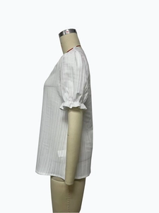 Detailed view of white short-sleeved shirt with vertical texture and ruffled cuffs