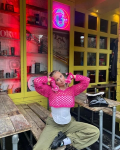 Outdoor shot of a pink hollow crochet knit sweater with flared sleeves and cargo pants