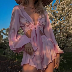 Pink satin two-piece set with tie-front long sleeve top and ruffled shorts in sunlight