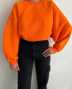Detalle de sudadera naranja de hombros caídos y pantalones cargo negros con bolsillos grandes