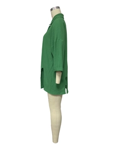 Detail of loose green shirt showing textured pleated fabric and side slit on a mannequin