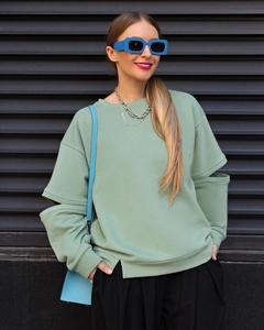 Détail d'un sweat-shirt vert clair avec une découpe unique sur les manches longues