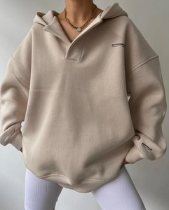 Détail d'un sweat à capuche beige oversize en polaire avec col en V et lettrage noir