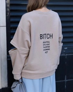 Détail d'un sweat-shirt beige avec manches découpées et impression de texte noir