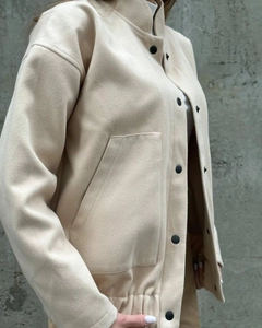Detail of beige jacket with stand collar, black buttons, and large side pockets