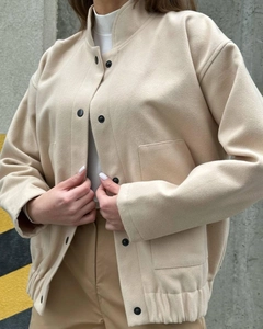 Detail of beige standing collar jacket with black snap buttons and large square pockets