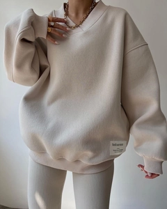 Detail of beige V-neck loose sweatshirt with ribbed cuffs and woven brand tag on hemline