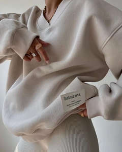 Close-up of cream oversized V-neck sweatshirt featuring ribbed cuffs and decorative patch
