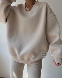 Detail view of beige oversized V-neck sweatshirt featuring ribbed edges and brand label