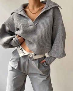 Details der grauen Strickstruktur des Polo-Pullovers mit goldenem Kettenaccessoire