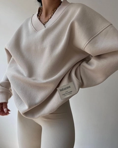 Detail view of woven brand label on the hem of a beige oversized V-neck sweatshirt