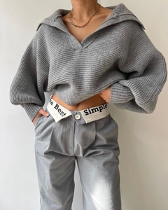 Detail eines grauen V-Ausschnitt Strickpullovers und einer Hose mit Taillenbeschriftung