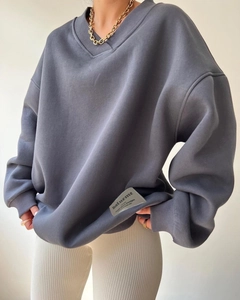 Close-up of a grey V-neck loose sweatshirt with ribbed cuffs and woven brand patch detail