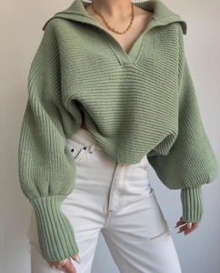 Detail eines salbeigrünen Grobstrickpullovers mit weitem Kragen und lockeren Ballonärmeln