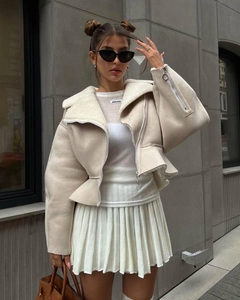 Detail of faux fur collar short jacket with zipper cuffs and pleated white mini skirt