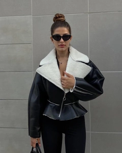 Detail of black faux leather biker jacket featuring white shearling lapel and peplum hem