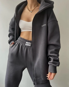 Detail of dark grey fleece hoodie and joggers set with white MAI STUDIOS embroidery