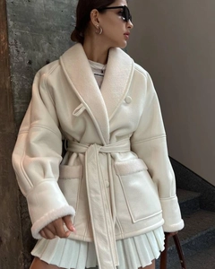 Detail of a creamy white patchwork faux fur coat featuring a large lapel and waist belt