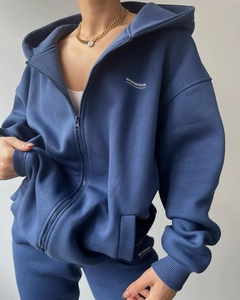 Detail of navy blue fleece-lined zip hoodie with white logo print and golden necklace