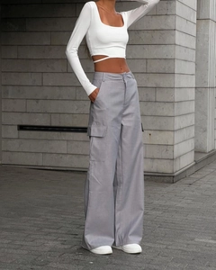 Close-up of white cropped long-sleeve top with cross-waist straps and grey cargo pants