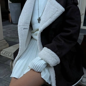 Détail d'une veste en similicuir fourrée avec collier croix et jupe en tricot