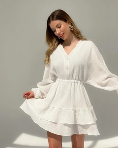 Detail of white V-neck dress featuring button accents and textured pleated fabric finish