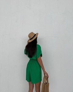 Detail of bright green casual romper with waist tie, straw hat and woven summer handbag