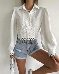 Close-up of white long sleeve shirt featuring intricate hollow lace trim and button detail