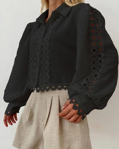 Close-up detail of a black long-sleeve blouse featuring intricate hollow-out lace trim