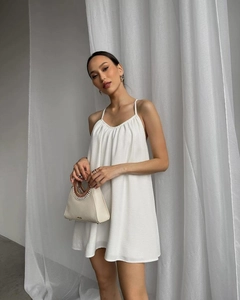 Close-up of white backless strap dress and beige handbag with woven handle in soft light