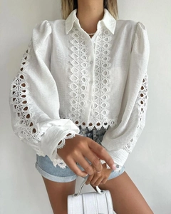 Detailed view of intricate white lace cutouts and hollow-out embroidery on a long sleeve shirt
