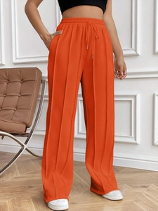 Détail du pantalon large orange vif avec plis verticaux et taille à cordon de serrage