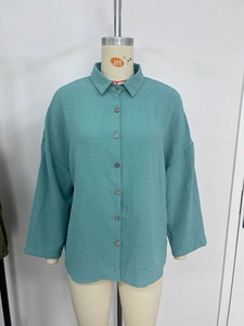 Detail of teal pleated shirt showing wood buttons, lapel collar, and textured fabric