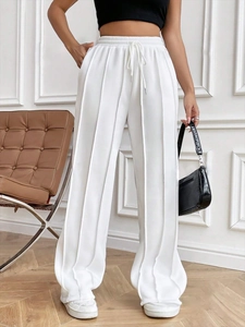 Détail du pantalon blanc à jambes larges avec plis verticaux et taille à cordon