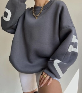 Detail of dark grey oversized hoodie with white sleeve lettering and gold accessories