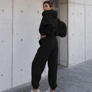 Outdoor street view showing the back profile of a loose black tracksuit with hoodie