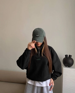 Detail of embroidered 'want' text on dark grey half-zip sweatshirt and vintage baseball cap