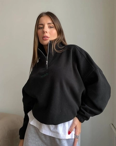 Detailed view of green want embroidery on a black half-zip oversized fleece sweatshirt
