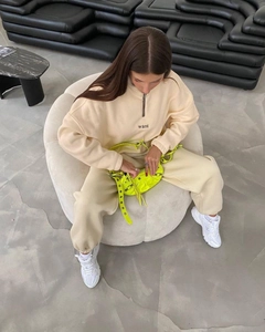 Detail of beige quarter-zip hoodie and matching sweatpants with neon yellow bag and sneakers