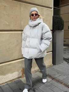 Street style shot of a loose light grey hooded puffer jacket with high collar for winter