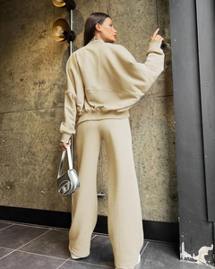Full back view of beige track jacket and wide-leg pants on model in industrial setting