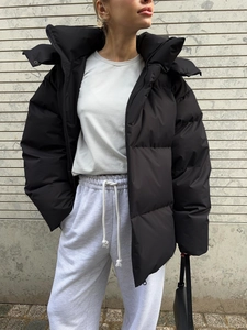 Detail of a black oversized hooded padded jacket with matte texture and wide quilting