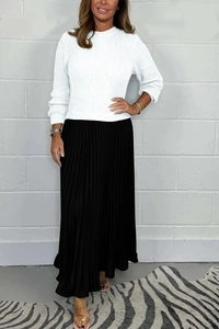 Detail view of a white knitted long sleeve sweater paired with a black pleated maxi skirt