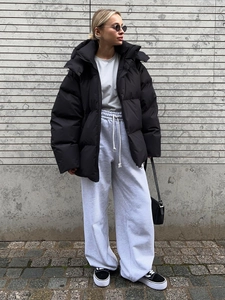 Outdoor street style view of a black oversized hooded puffer jacket and grey joggers