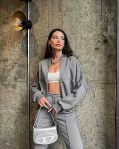 Detail of grey zip-up hoodie set with silver D-logo handbag and industrial background
