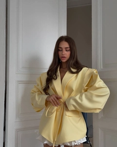 Detail of light yellow blazer featuring padded shoulders and a waist-tie belt closure