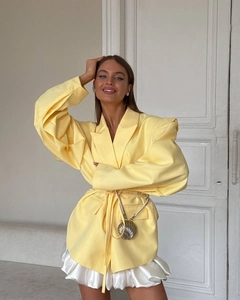 Detailed view of yellow waist-tie blazer with shoulder pads and shell crossbody bag